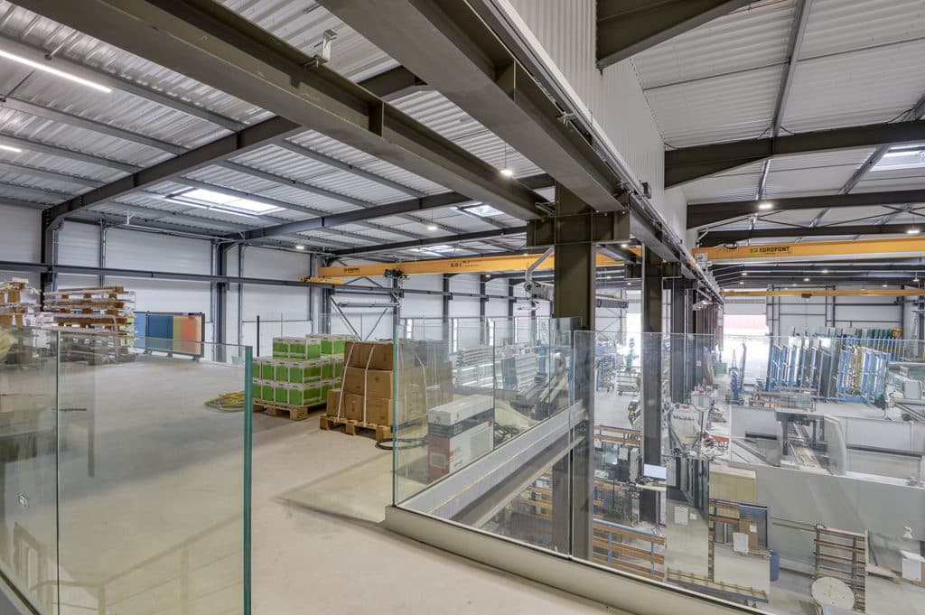 Vue intérieure de l'atelier VERTIGE — ponts roulants, racks de stockage du verre, postes de façonnage